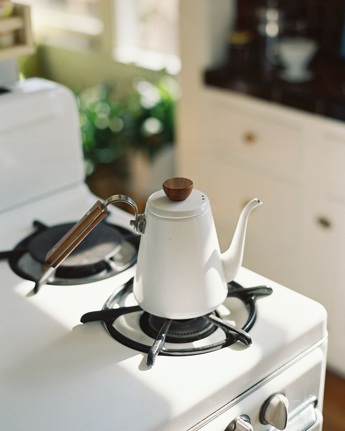 A white enamel kettle by Bona with a wooden handle on a white stove